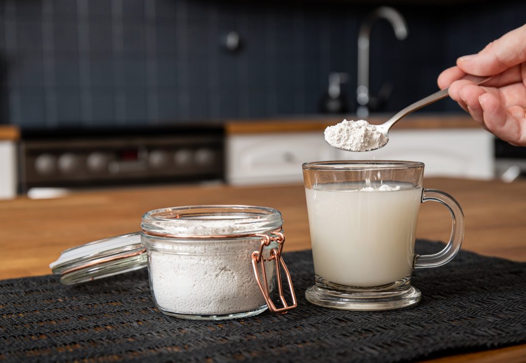 Diatomaceous earth also known as diatomite mixed in glass of water, good for human body detox concept. Jar and glass with healthy drink on home kitchen table.