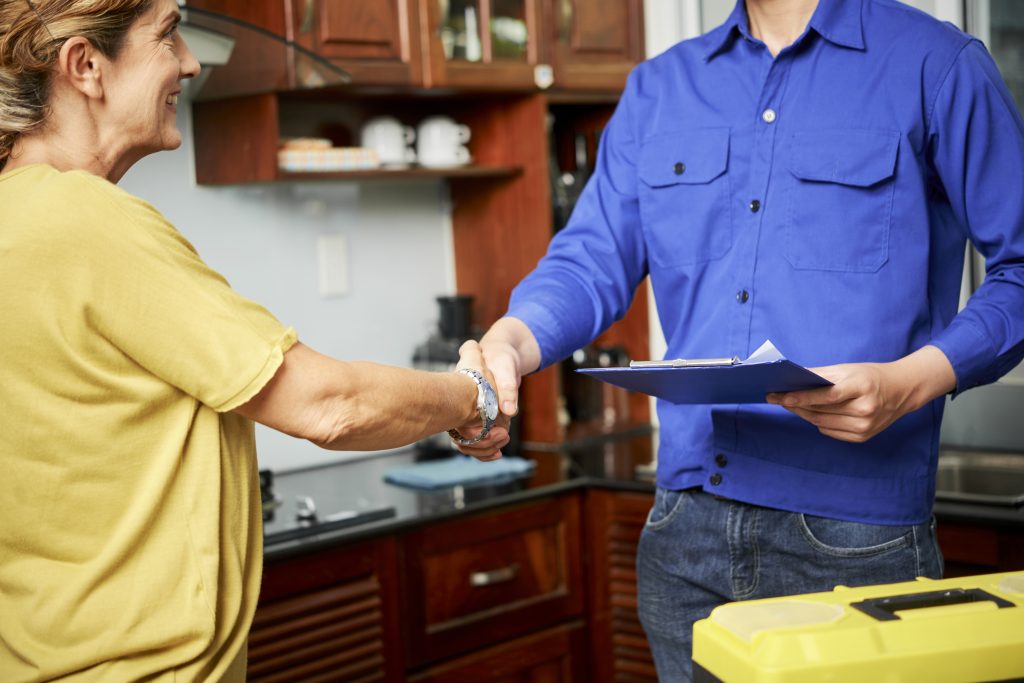 Happy mature woman shaking hand of plumber who fixed sink leak from drain