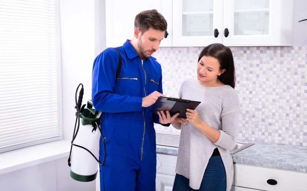Young Male Pest Control Worker Showing Invoice To Woman In Domestic Kitchen