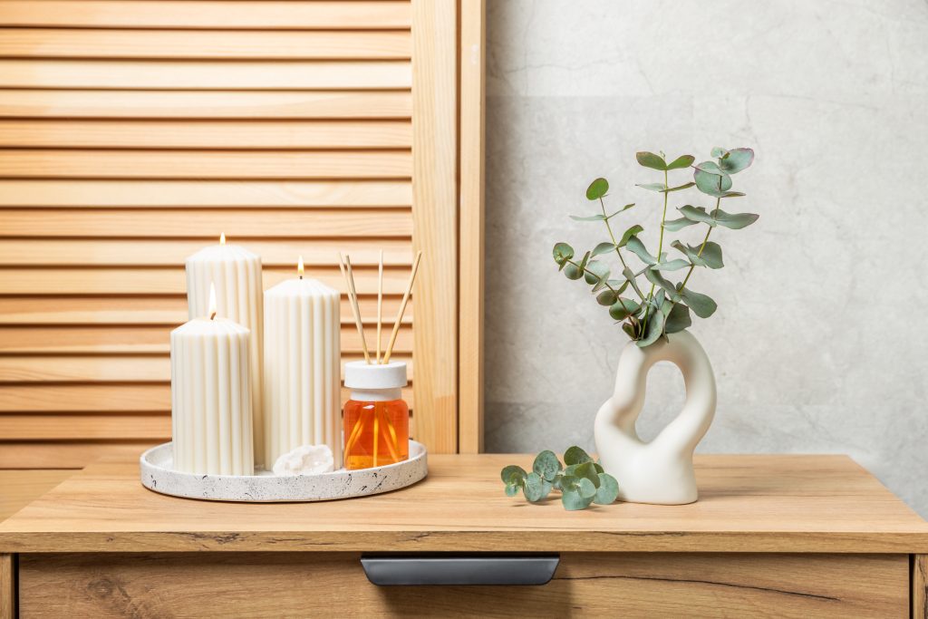 Green eucalyptus leaves in a vase stand on a chest of drawers against the background of a wall. Aromatherapy.Beautiful eucalyptus bouquet.Minimalist interior with flowers, candles and aroma diffuser.