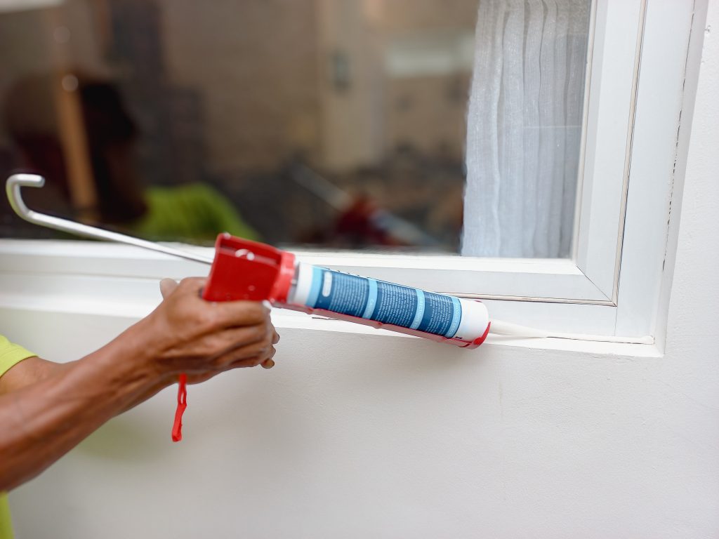 Construction worker using silicone sealant caulk the outside window frame. Hands Applying Weather Seal Caulk to Window Frame.
